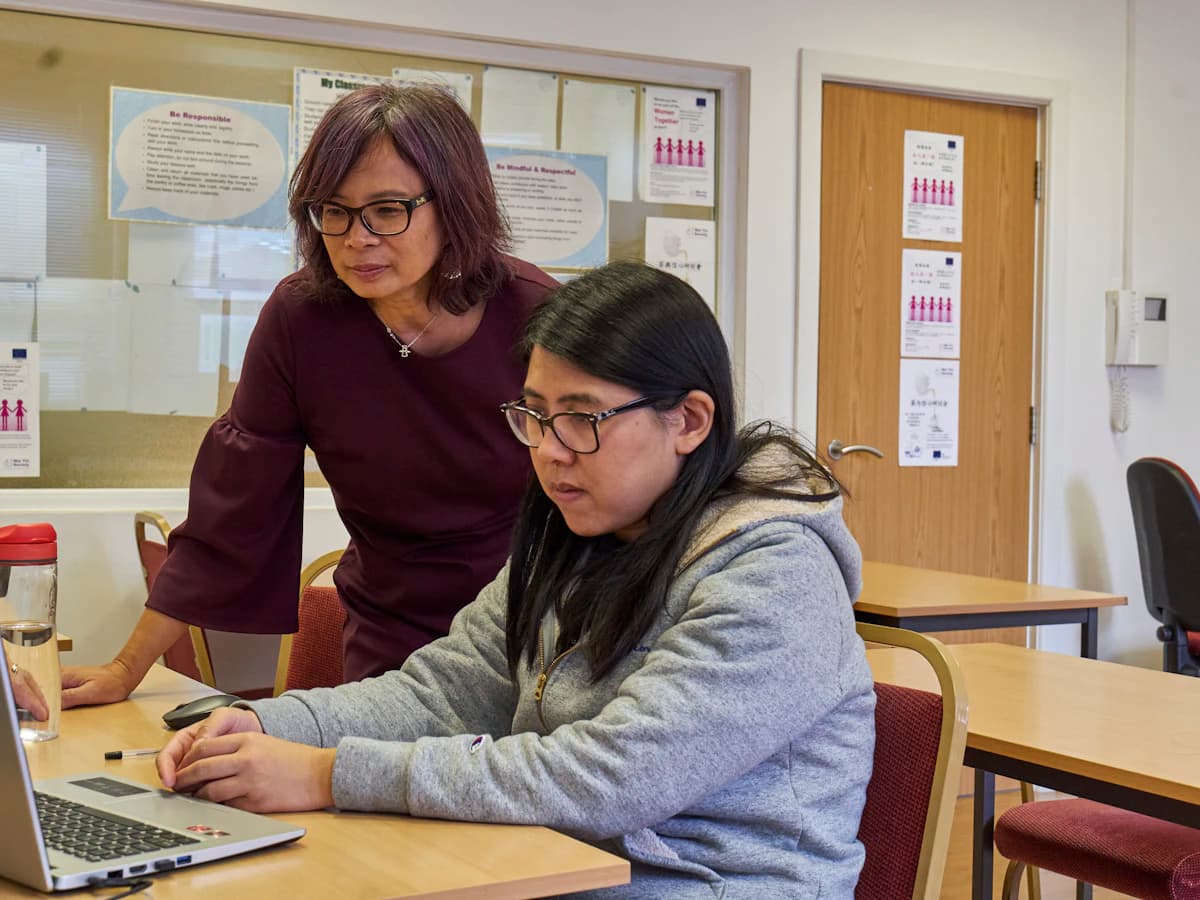 Una profesora ayudando a una alumna frente a una computadora
